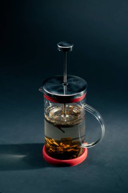 Koyu mavi arka planda, yan ışıklandırmayla birlikte yeşil çay demleyen modern bir çaydanlık var.