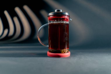 Koyu mavi bir arka planda, yan ışıklandırması olan modern bir çaydanlık, üzerinde yüzen siyah çay yaprakları demlemek için baskı yapıyor.