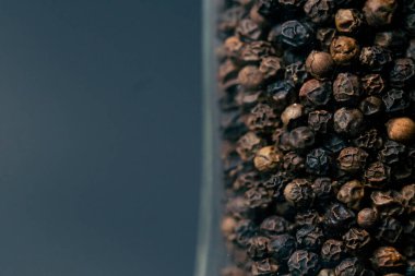 Yan ışıklandırması olan koyu mavi bir arkaplanda farklı büyük biber restoranlarının sunduğu cam biber karıştırıcı duruyor.