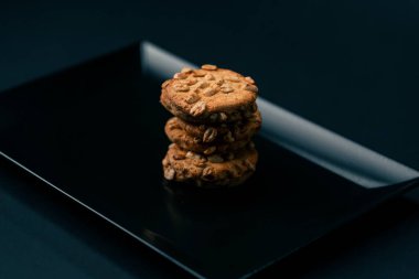 Siyah ve mavi arka planda düz siyah bir tabakta. Piramit şeklinde kurabiyeler var. Mutfak temiz.