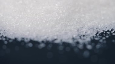 Siyah-mavi arka planda yakın plan beyaz granüle şeker uzanıyor, şeker yığınının etrafındaki kristal topaklar sağlığa zararlıdır