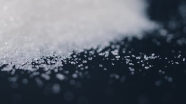 Siyah-mavi arka planda yakın plan beyaz granüle şeker uzanıyor, şeker yığınının etrafındaki kristal topaklar sağlığa zararlıdır