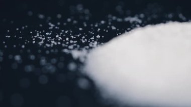 Siyah-mavi arka planda yakın plan beyaz granüle şeker uzanıyor, şeker yığınının etrafındaki kristal topaklar sağlığa zararlıdır