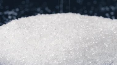 Siyah-mavi arka planda yakın plan beyaz granüle şeker kristalleri üzerine uzanır. Sağlığa zararlı bir slayta dökülür.