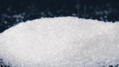 Siyah-mavi arka planda yakın plan beyaz granüle şeker kristalleri üzerine uzanır. Sağlığa zararlı bir slayta dökülür.
