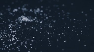 Siyah-mavi arka planda yakın plan beyaz granüle şeker uzanıyor, şeker yığınının etrafındaki kristal topaklar sağlığa zararlıdır