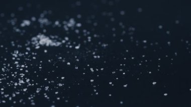 Siyah-mavi arka planda yakın plan beyaz granüle şeker uzanıyor, şeker yığınının etrafındaki kristal topaklar sağlığa zararlıdır