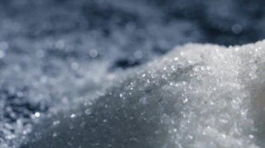 Siyah-mavi arka planda yakın plan beyaz granüle şeker kristalleri üzerine uzanır. Sağlığa zararlı bir slayta dökülür.