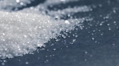 Siyah-mavi arka planda yakın plan beyaz granüle şeker kristalleri üzerine uzanır. Sağlığa zararlı bir slayta dökülür.