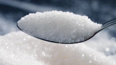 Siyah-mavi arka planda yakın plan beyaz granüle şeker uzanıyor üzerinde kristal şeker sağlığa zararlı bir kaşıktan dökülüyor