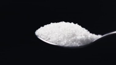 Siyah-mavi arka planda yakın plan beyaz granüle şeker uzanıyor üzerinde kristal şeker sağlığa zararlı bir kaşıktan dökülüyor