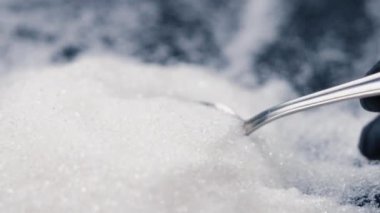 Siyah-mavi arka planda yakın plan beyaz granüle şeker uzanıyor üzerinde kristal şeker sağlığa zararlı bir kaşıktan dökülüyor