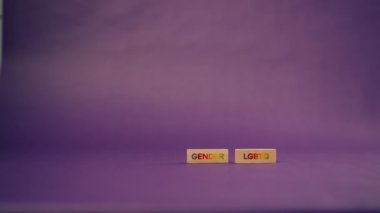 Siyah harfli tahtadan küplerle mor, sıcak bir arkaplan ve LGBTQ harflerinin renklerinden sözcükler sergiliyor.