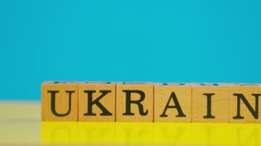 Ukrayna bayrağı mavi ve sarı sıcacık arkaplan ve gölgeli kadın eli siyah harfli ahşap küpler koydu.