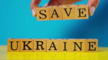 Ukrayna bayrağı mavi ve sarı sıcak arka plan, gölgeli kadın eli, siyah harfli ahşap küpler, Ukrayna 'yı kurtar.