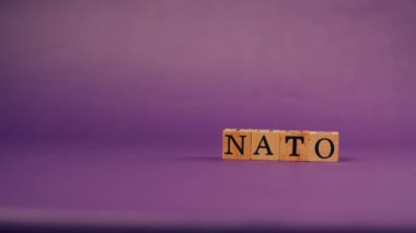 Siyah harfli, gölgeli tahta küplerle mor, ılık bir arka plan ve NATO harflerinden kelimeler.