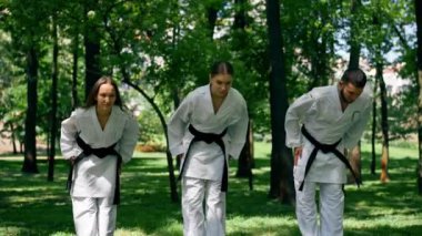 Parkta açık havada güneşli hava genç karatekalar karate tekniğini kullanarak ısınıyor. Kara kuşak sağlıklı yaşam tarzı eğitimi.