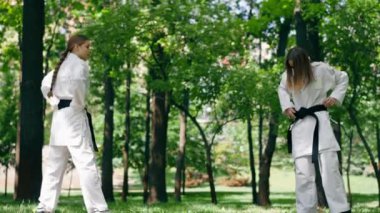 Parkta açık havada, güneşli havada genç bir karateci kız. Trenin çevikliği ve tepkisi. Siyah kuşakla oynayan bir top dövüş sanatları oyuncusuyla oynuyor.