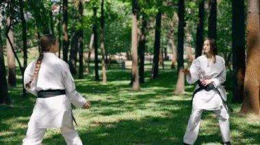 Parkta açık havada, güneşli havada genç bir karateci kız. Trenin çevikliği ve tepkisi. Siyah kuşakla oynayan bir top dövüş sanatları oyuncusuyla oynuyor.