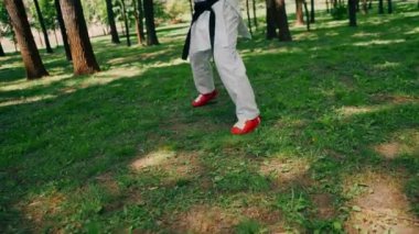 Parkta açık havada, güneşli havada kırmızı asker botları ve eldiven giymiş genç bir karateci tekniklerini uyguluyor.