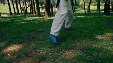 Parkta açık havada, güneşli havada mavi çizme ve eldiven giymiş genç bir karateci kız tekniklerini uyguluyor.