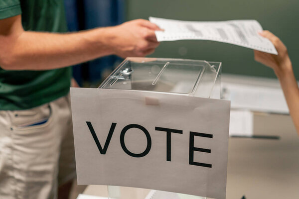 В отборочной комиссии избирательной кампании парень регистрируется для голосования, молодая девушка рассказывает, как голосовать раздавая бюллетень для голосования