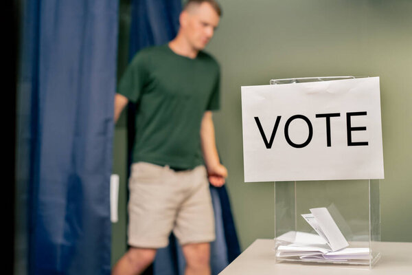 в избирательном округе на президентских выборах молодой человек, который проголосовал выходит из синей будки с бюллетенем