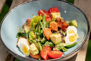 Üst çekim, caddedeki bir restoranda, bir tahta masanın üzerinde. Avokado ve güneş ışınlarında karides içeren sıcak bir salatayla mavi bir tabak.
