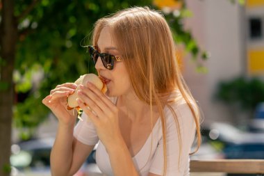 Caddedeki bir restoranda güneş gözlüklü güzel, uzun saçlı bir kız bir masada oturmuş öğle yemeği yiyor.