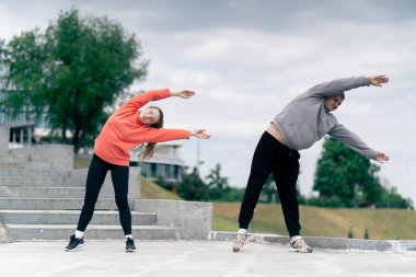 Parkta birbirine aşık genç bir çift spor yapıyor. Sağlıklı yaşam tarzı senkronize hareketleri ısıtıyor.