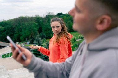 Parkta spordan sonra aşık olan genç bir çift telefonda turuncu kapüşonlu kıza mesaj atıyor.