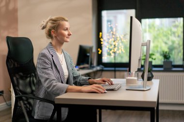 Beyaz duvarlı parlak bir ofiste genç sarışın bir çalışan beyaz bir ekranda çalışıyor modern ofis güneş ışınları bir proje üzerinde çalışıyor.