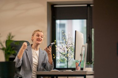 Aydınlık bir ofiste sarışın genç bir çalışan beyaz bir monitörde çalışıyor.