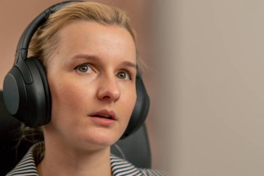 Aydınlık bir ofiste genç bir sarışın beyaz bir ekranda çalışıyor modern ofis güneş ışınları büyük siyah kulaklıklar üzerinde çalışıyor.