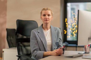 Aydınlık bir ofiste genç sarışın bir çalışan beyaz bir ekranda çalışıyor. Modern bir ofis kameraya bakıyor.