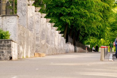 Aşağıya doğru eğimli beton bir duvarı olan güzel, temiz bir kaldırım. Dikilmiş ağaçlar, çitlerle çevrili bir alan.