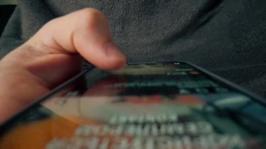 Yukarıdan, erkeğin elini kaydırdığı ve sosyal ağlarda teknolojik ilerleme kaydettiği bir cep telefonunun çapraz görüntüsü
