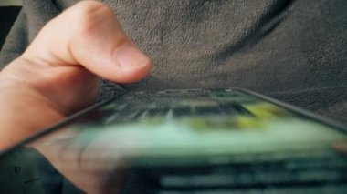 Yukarıdan, erkeğin elini kaydırdığı ve sosyal ağlarda teknolojik ilerleme kaydettiği bir cep telefonunun çapraz görüntüsü