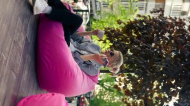 dikey video ofis kıyafetleri içinde pembe bir kız terasta güneş gözlüğü takıyor ve telefonda hoparlörden konuşuyor.