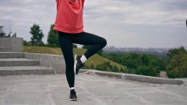 Parkta turuncu kapüşonlu genç bir kız ısınıyor sağlıklı bir yaşam tarzı meditasyon yapıyor bulutlu bir havada duruyor.