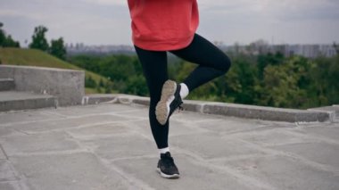 Parkta turuncu kapüşonlu genç bir kız ısınıyor sağlıklı bir yaşam tarzı meditasyon yapıyor bulutlu bir havada duruyor.