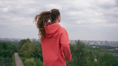 Parkta turuncu kapüşonlu genç bir kız ısınıyor sağlıklı bir yaşam tarzı meditasyon yapıyor bulutlu bir havada duruyor.