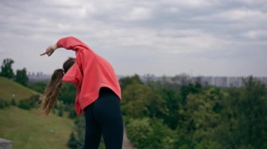 Parkta turuncu kapüşonlu genç bir kız ısınıyor sağlıklı bir yaşam tarzı meditasyon yapıyor bulutlu bir havada duruyor.