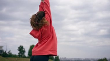 Parkta turuncu kapüşonlu genç bir kız ısınıyor sağlıklı bir yaşam tarzı meditasyon yapıyor bulutlu bir havada duruyor.