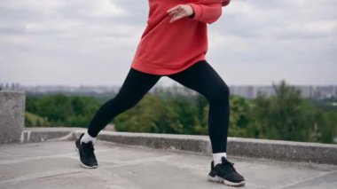 Parkta turuncu kapüşonlu genç bir kız ısınıyor sağlıklı bir yaşam tarzı meditasyon yapıyor bulutlu bir havada duruyor.