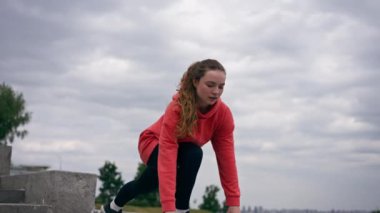 Parkta turuncu kapüşonlu genç bir kız ısınıyor sağlıklı bir yaşam tarzı meditasyon yapıyor bulutlu bir havada duruyor.