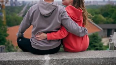 Parkta birbirine aşık genç bir çift, spor yaptıktan sonra beton korkuluklara sarılıyor, şehri seyrediyor, bulutlu bir hafta sonu.