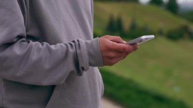 Gri kapüşonlu spor yaptıktan sonra parktaki adam telefonda sağlıklı yaşam tarzıyla mesajlaşıyor.
