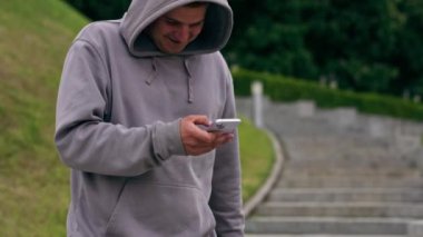 Parkta spor yaptıktan sonra gri kapüşonlu adam telefonda mesaj atıyor. Aktif, sağlıklı yaşam tarzı.