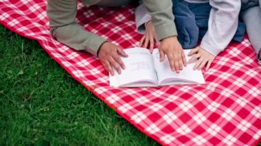 Parkta kalın elbiseli bir adam ve kız, mavi bir battaniyeyle kaplı bir battaniyenin üzerinde kitap okuyan bir kıza sarılıyorlar.